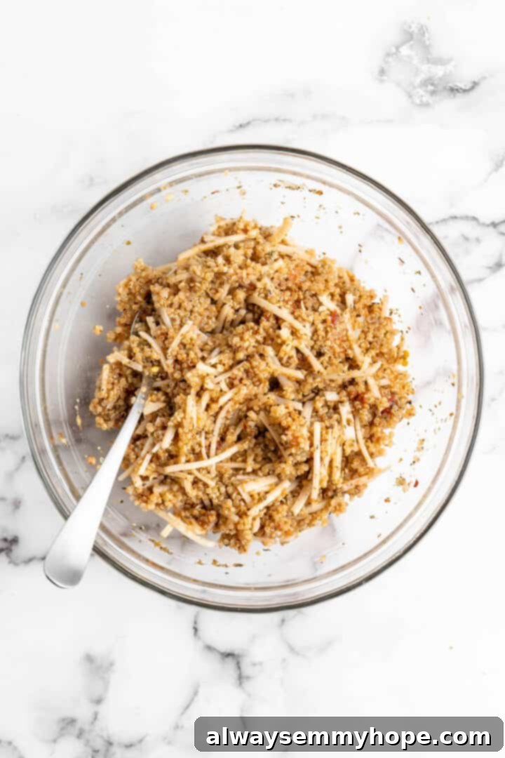 The cohesive quinoa pizza bite mixture, perfectly seasoned and ready for the muffin pan. Quinoa pizza bite mixture in a glass bowl with a spoon, showing its ready-to-fill consistency