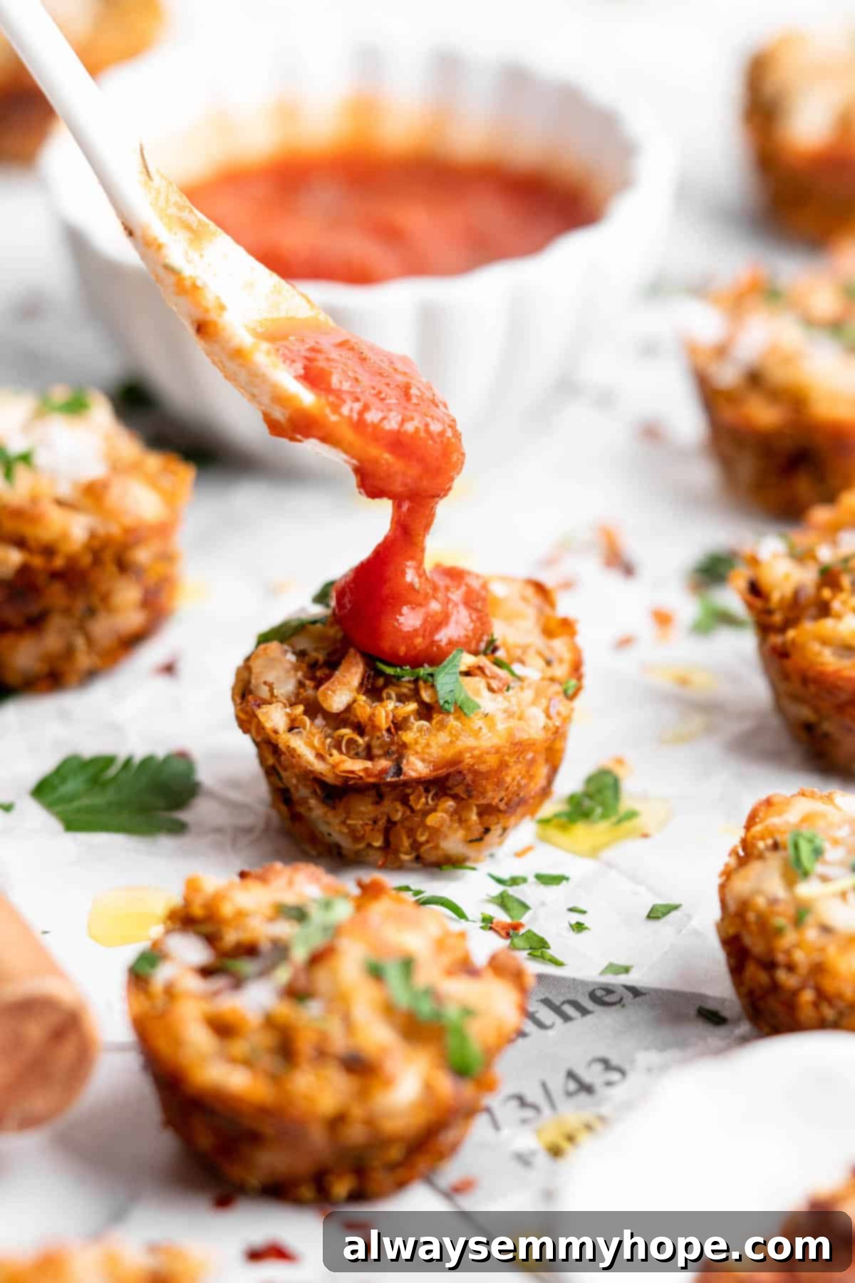 Enhance your Quinoa Pizza Bite with a generous dollop of marinara sauce. Close-up of a hand spooning marinara sauce over a quinoa pizza bite, emphasizing the delicious topping