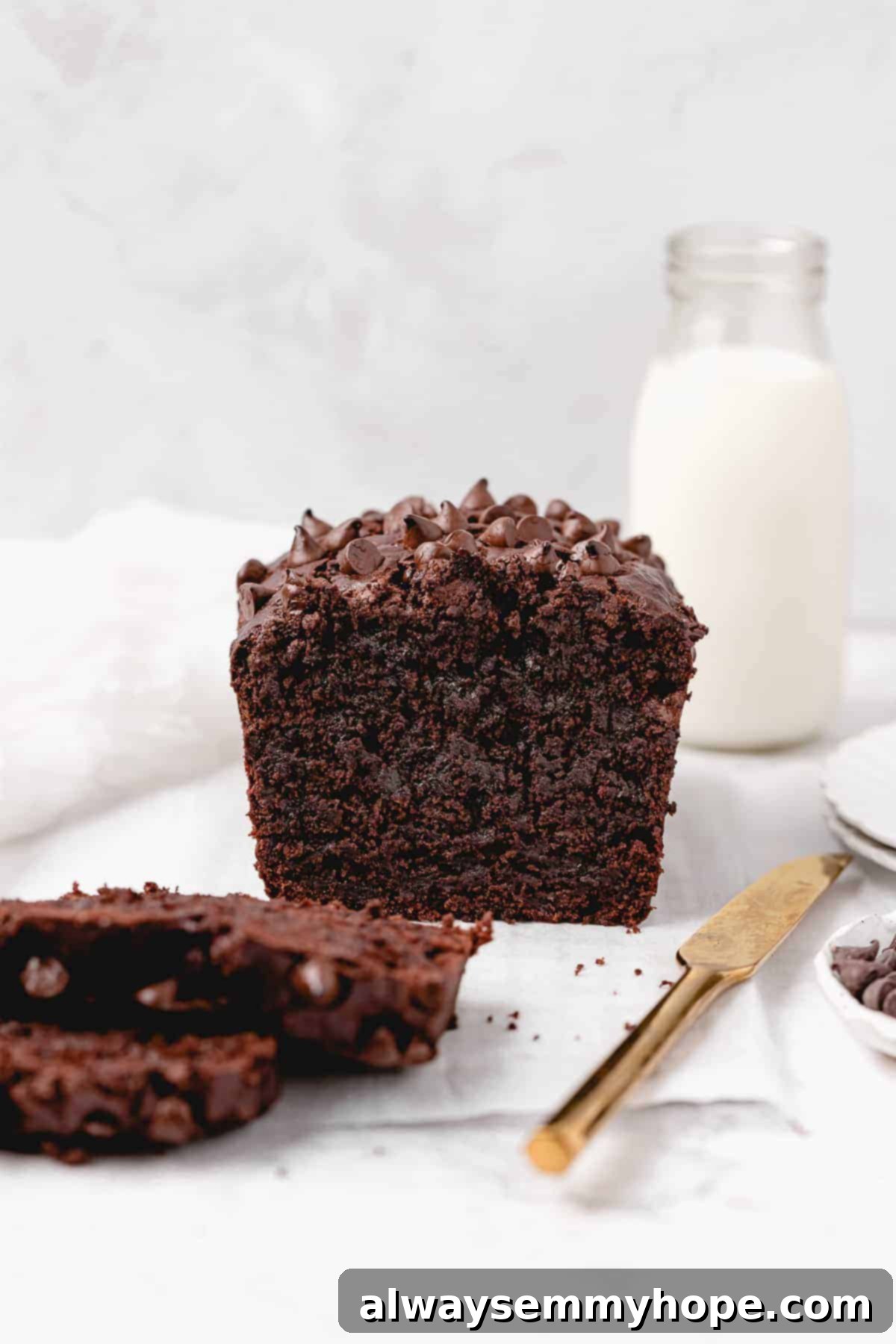 Fudgy Vegan Chocolate Banana Bread 3 Sliced loaf of chocolate banana bread with a jar of vegan milk on a rustic wooden board.