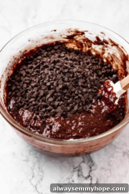 Fudgy Vegan Chocolate Banana Bread 9 Mini chocolate chips sprinkled on top of banana bread batter in a mixing bowl, ready to be folded in.