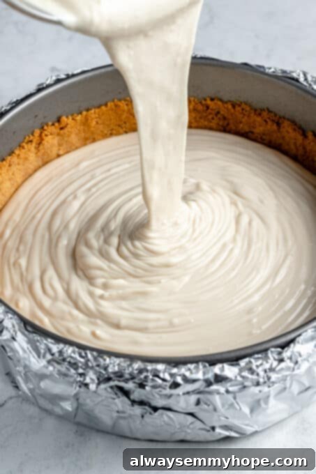 Smooth vanilla cheesecake filling being poured carefully over the baked graham cracker crust in a springform pan.
