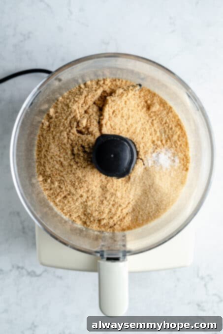 Graham cracker crumbs and brown sugar being processed in a food processor, creating the base for the cheesecake crust.