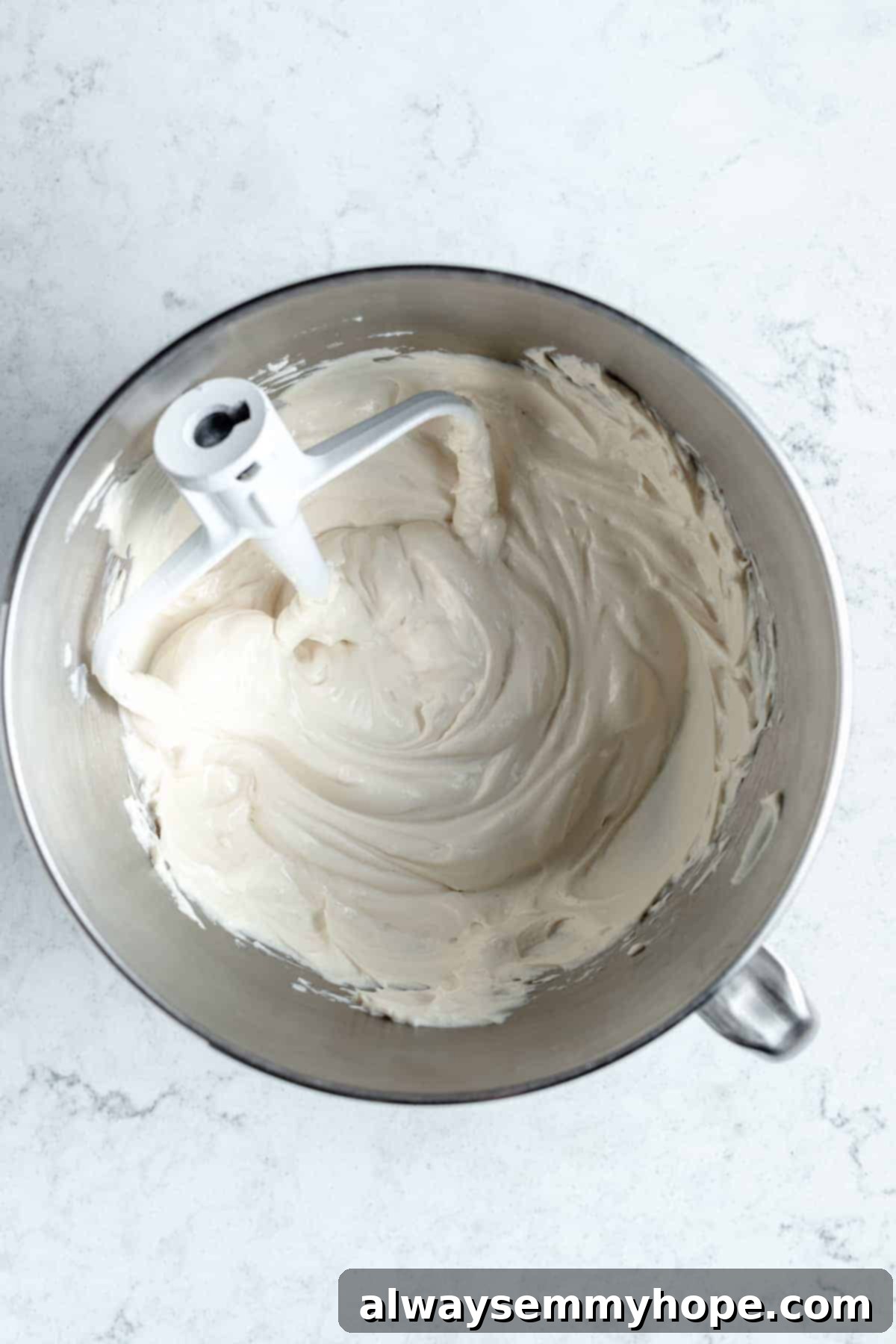 Creamy vegan cream cheese being beaten in a stand mixer bowl, becoming smooth and ready for other ingredients.