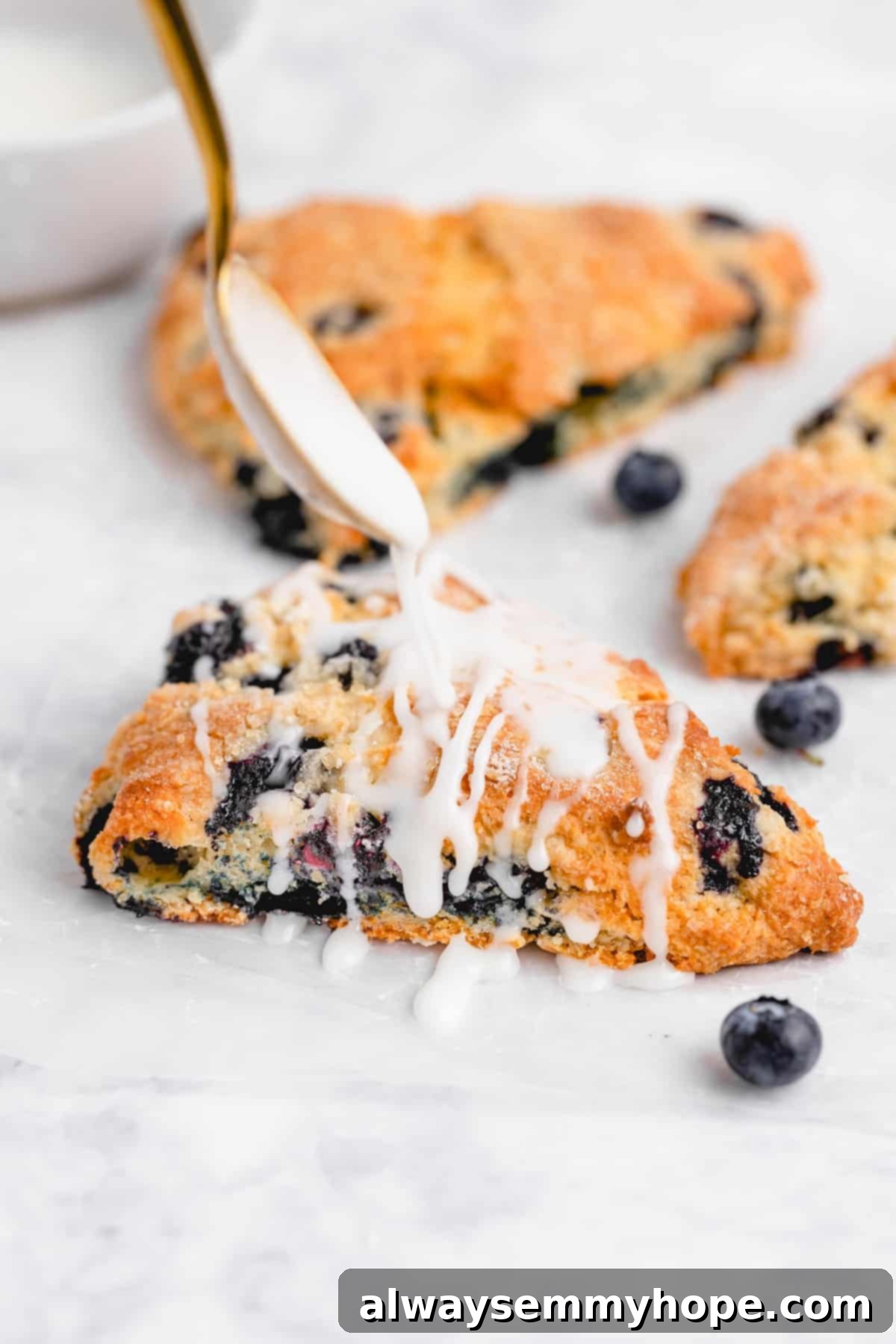 Fluffy Vegan Scones 2 White glaze being drizzled onto a perfectly baked blueberry vegan scone, showcasing its moist interior