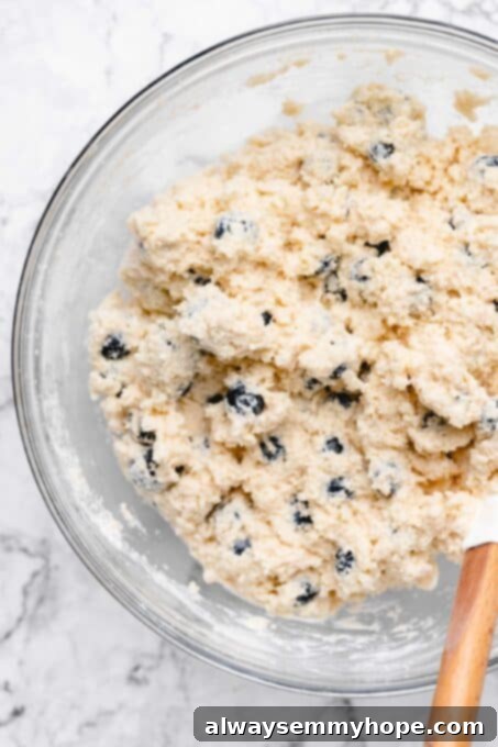 Fluffy Vegan Scones 8 More close-up of a spatula mixing blueberries into scone dough in a bowl, showing the shaggy texture