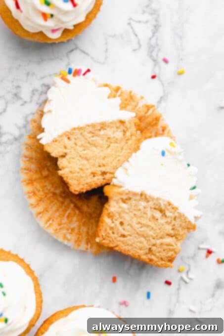 A vegan vanilla cupcake sliced in half, revealing its moist, fluffy interior and creamy frosting.