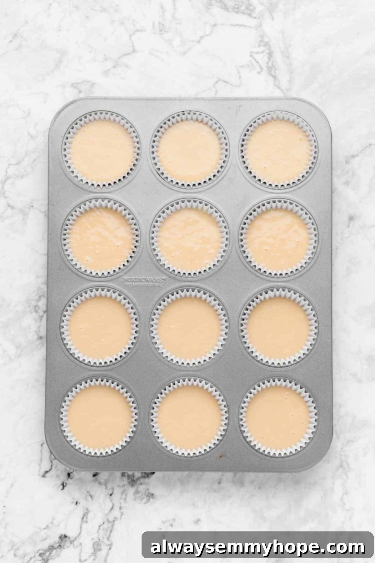 Cupcake pan with liners filled halfway with vanilla batter, ready for baking.