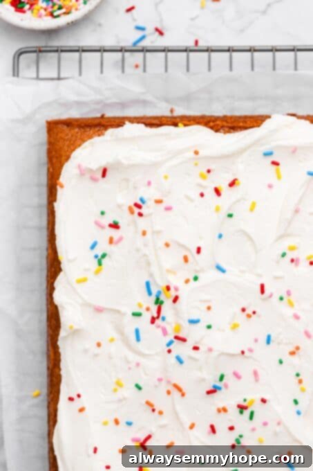 A whole vegan vanilla sheet cake with whipped frosting, topped with a cascade of rainbow sprinkles.