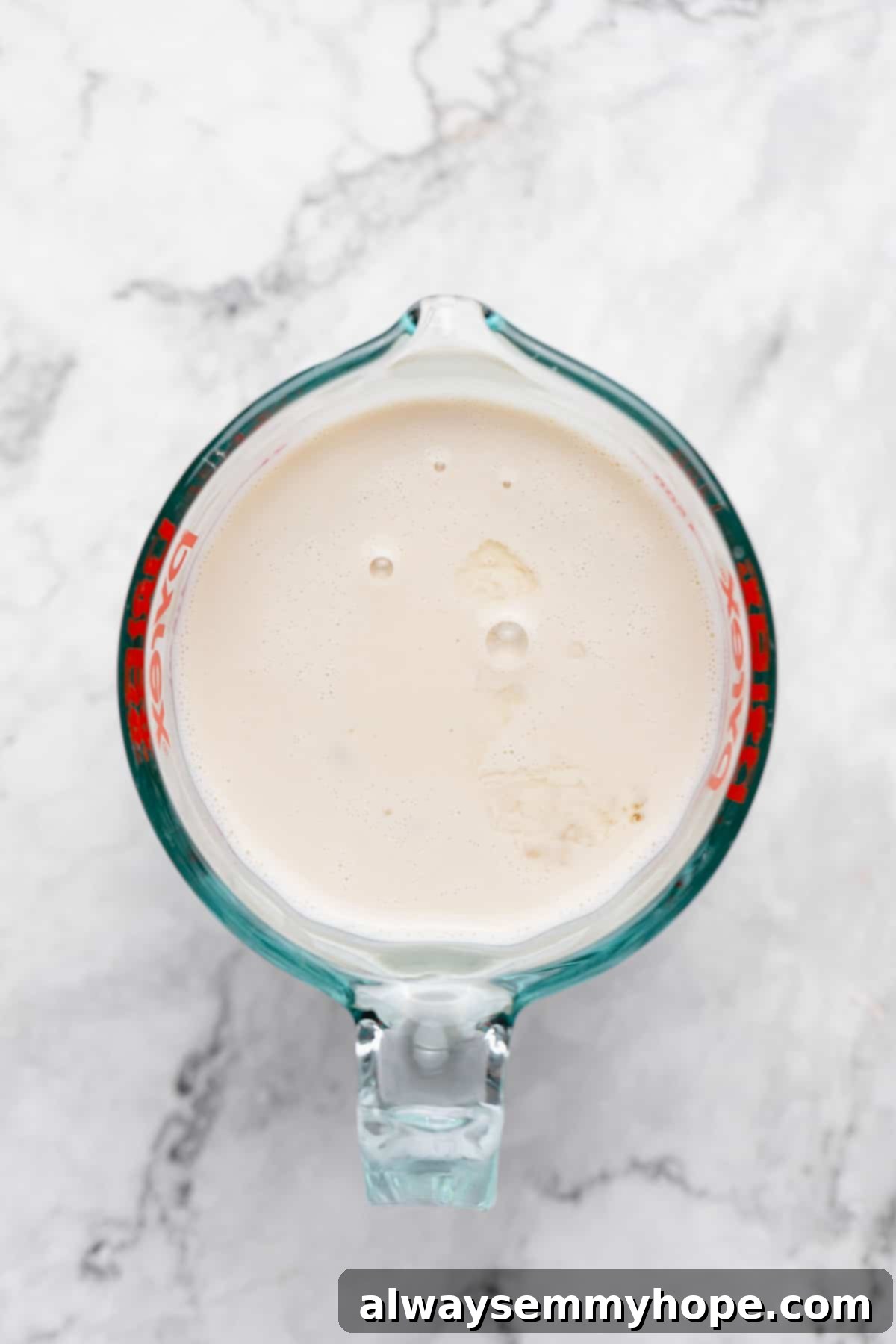 Soy milk and apple cider vinegar mixing in a clear measuring cup, showing the curdling process for vegan buttermilk.