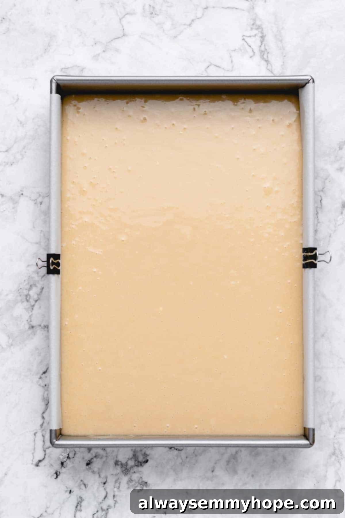 Vanilla cake batter evenly spread in a prepared sheet pan, ready to bake.