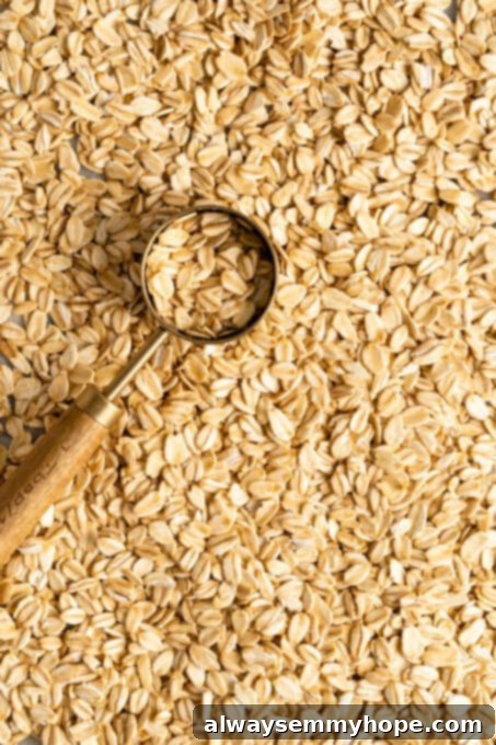 Dry rolled oats displayed on a wooden board, with a measuring cup to the side, ready for portioning. Oats are a popular whole grain, valued for their fiber content and as a source of plant-based protein, especially in breakfast meals.