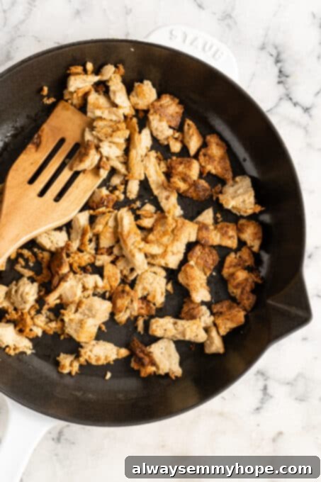 A generous portion of cooked seitan, made from vital wheat gluten, in a cast iron pan with a wooden spatula. Seitan is a chewy, protein-dense vegan meat substitute, ideal for mimicking the texture of meat in various recipes.
