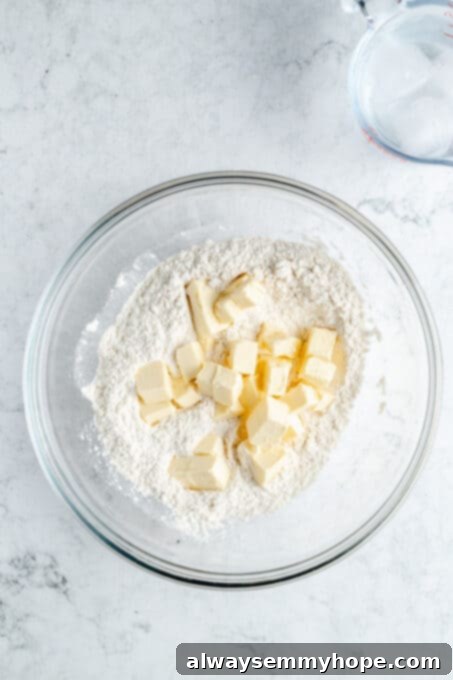A bowl filled with sifted flour, with small cubes of very cold vegan butter added on top, ready for mixing.