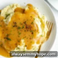 Ultimate Vegan Gravy 2 Overhead shot of creamy mashed potatoes on a white plate generously topped with rich vegan gravy and garnished with fresh herbs.