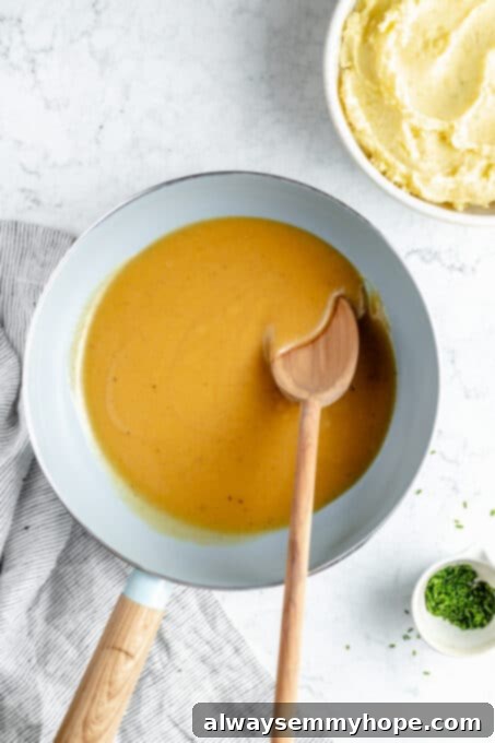 This vegan gravy is easy to make, silky smooth and delicious over mashed potatoes! It's packed with savoury flavour, made without mushrooms. Thickened vegan gravy simmering in a saucepan with a wooden spoon, ready to serve.