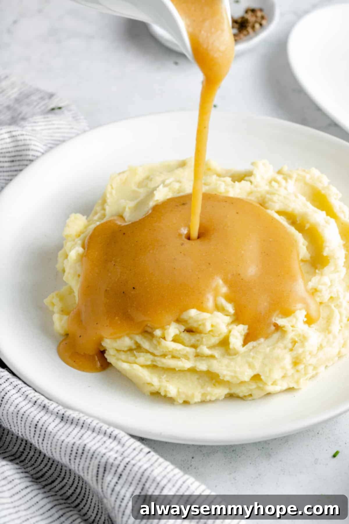 This vegan gravy is easy to make, silky smooth, and delicious over mashed potatoes! It's packed with savoury flavour, made without mushrooms. Rich vegan gravy being poured from a white gravy boat onto a bed of fluffy mashed potatoes.
