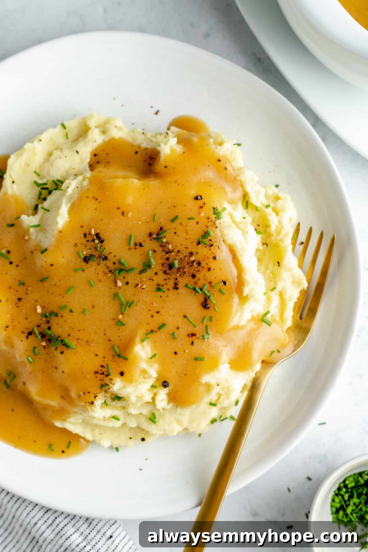 This vegan gravy is easy to make, silky smooth, and delicious over mashed potatoes! It's packed with savoury flavour, made without mushrooms. Overhead shot of perfectly mashed potatoes on a pristine white plate, generously coated with velvety smooth vegan gravy.