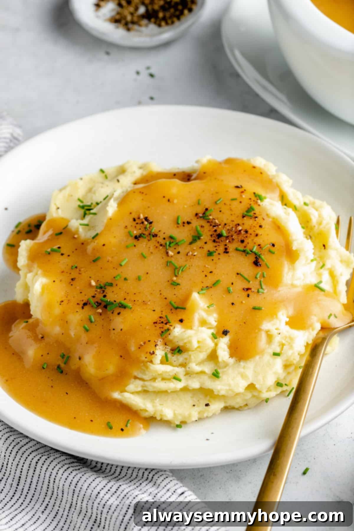 This vegan gravy is easy to make, silky smooth, and delicious over mashed potatoes! It's packed with savoury flavour, made without mushrooms. Creamy mashed potatoes on a white plate, covered with rich vegan gravy and elegantly topped with a sprinkle of minced fresh herbs.