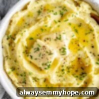Overhead shot of Vegan Mashed Potatoes in bowl topped with two pats of butter and minced herbs