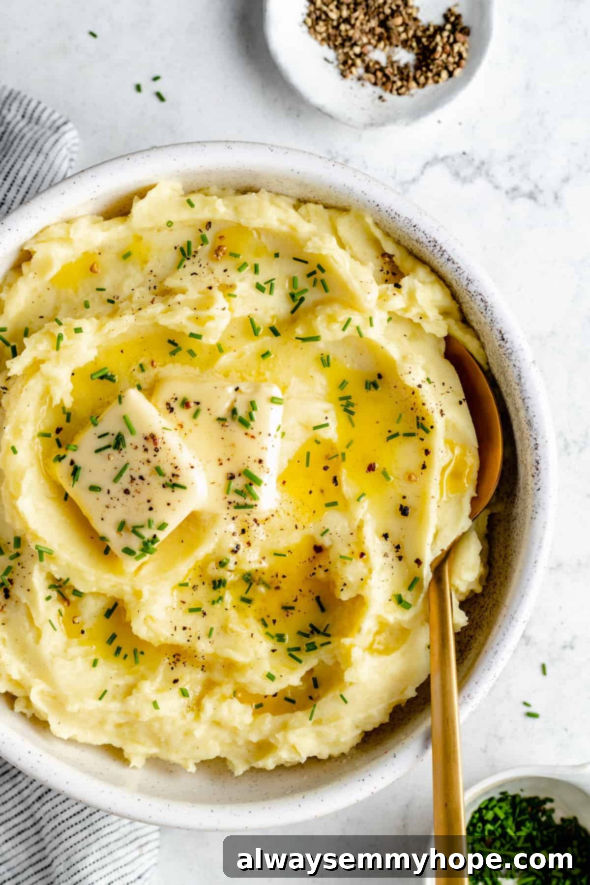 Overhead shot of mashed potatoes in bowl topped with pats of butter and herbs