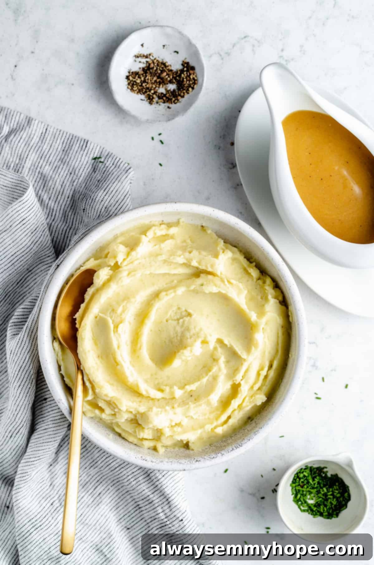 Overhead shot of bowl of Vegan Mashed Potatoes, gravy boat, and garnishes