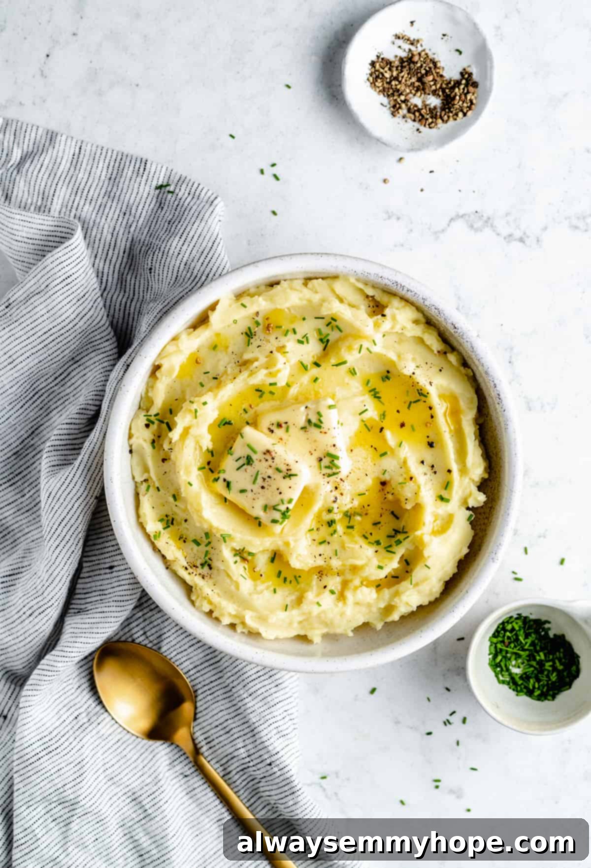 Overhead shot of Vegan Mashed Potatoes in serving bowl with gold spoon and small bowls of garnishes