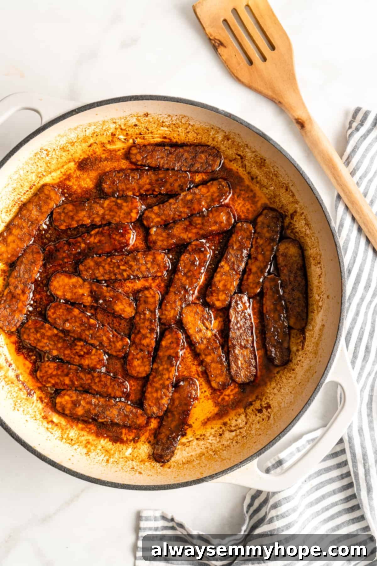 Crispy tempeh bacon slices cooking in a cast iron Dutch oven, highlighting their golden-brown edges