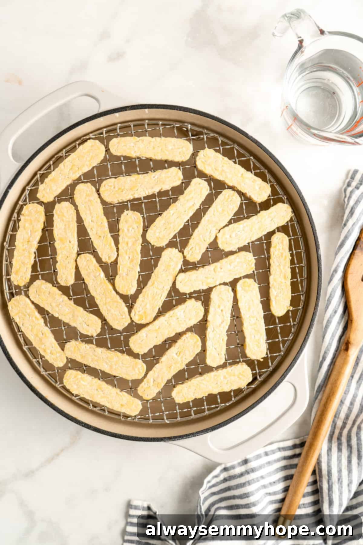 Tempeh slices steaming in a Dutch oven with a steamer basket, preparing them for marinade absorption.