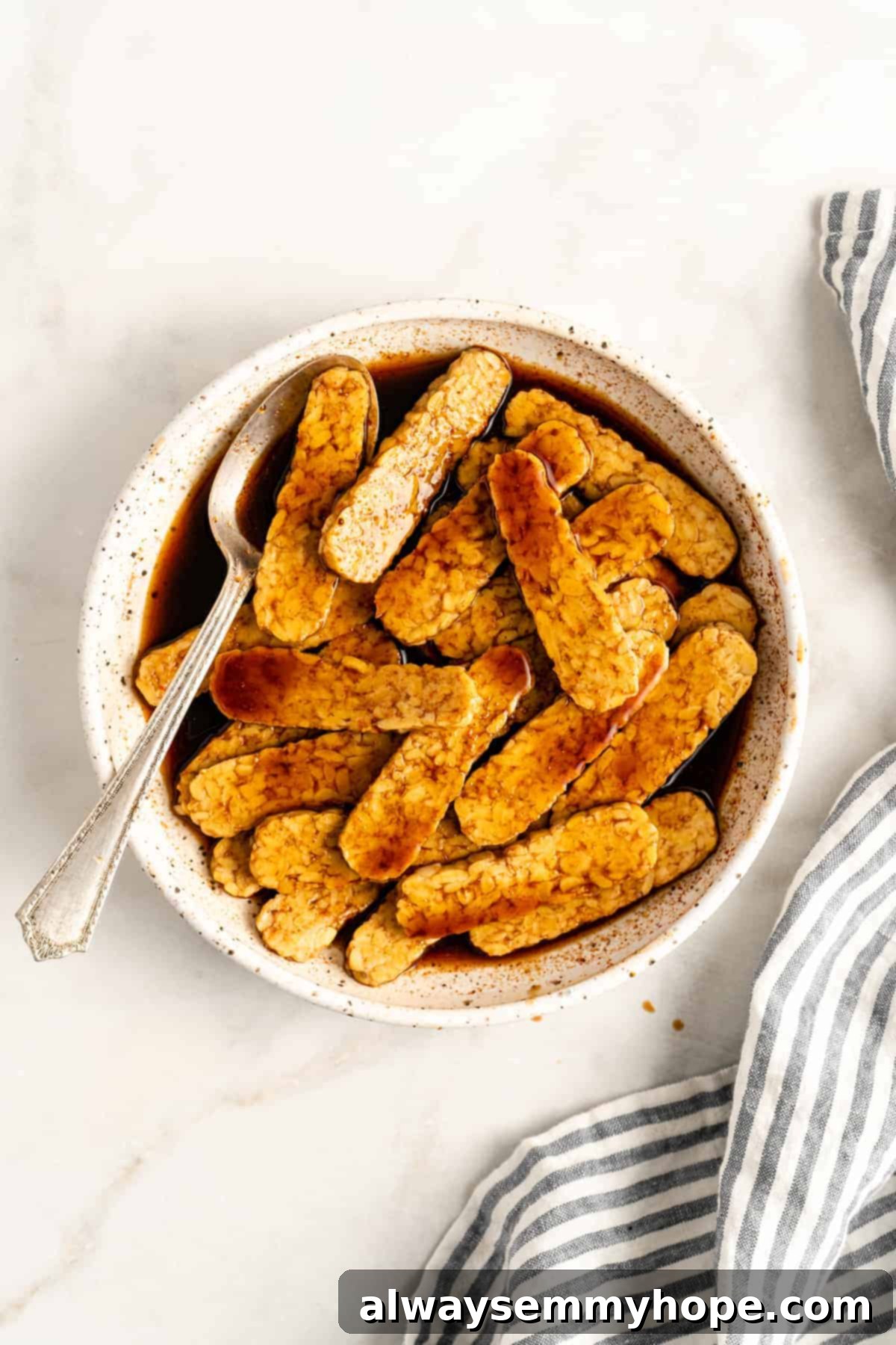 Bowl of steamed tempeh slices soaking in a dark, rich marinade, ready for refrigeration.