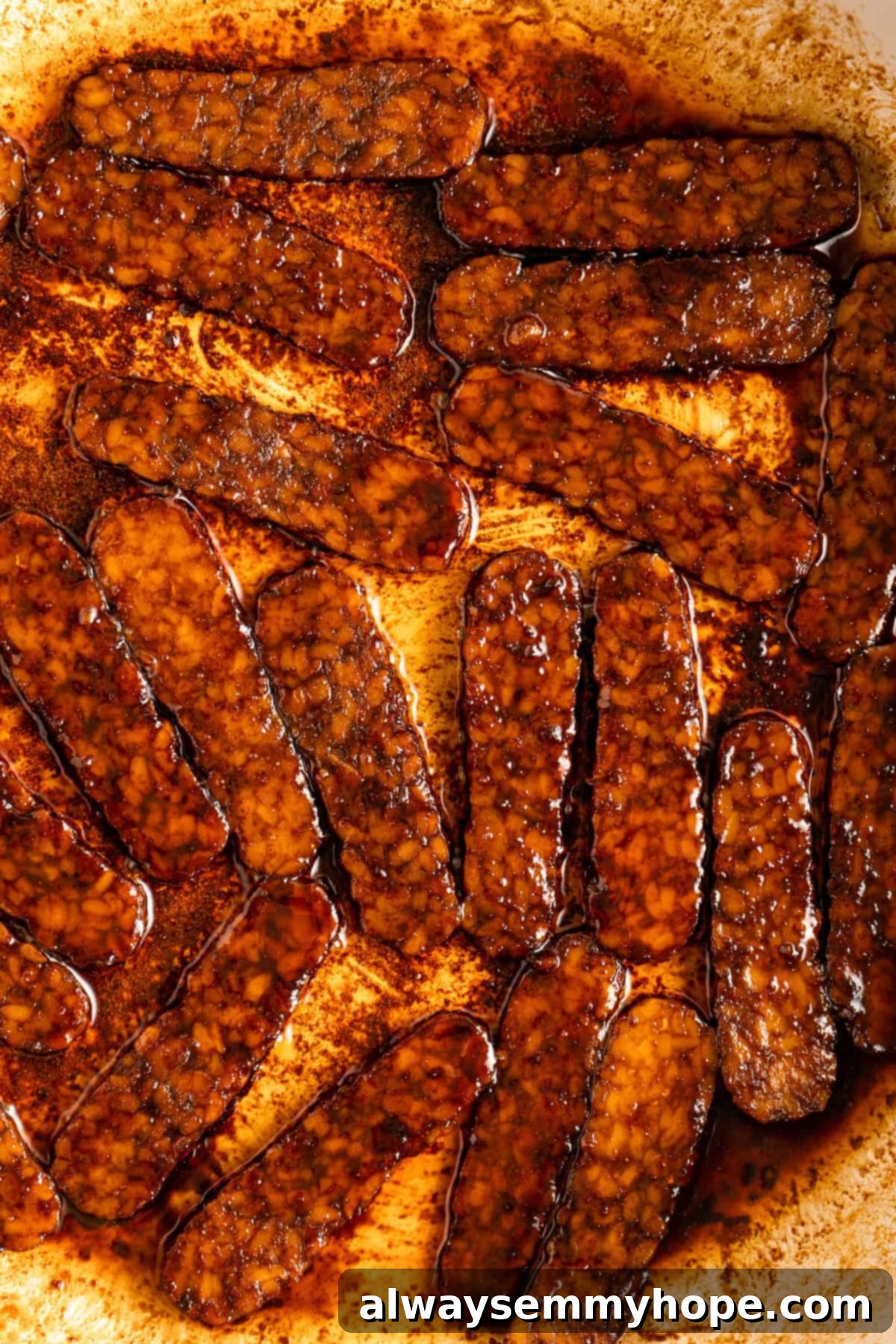 Closeup of tempeh bacon slices sizzling and browning in a hot skillet, showing their crispy texture.