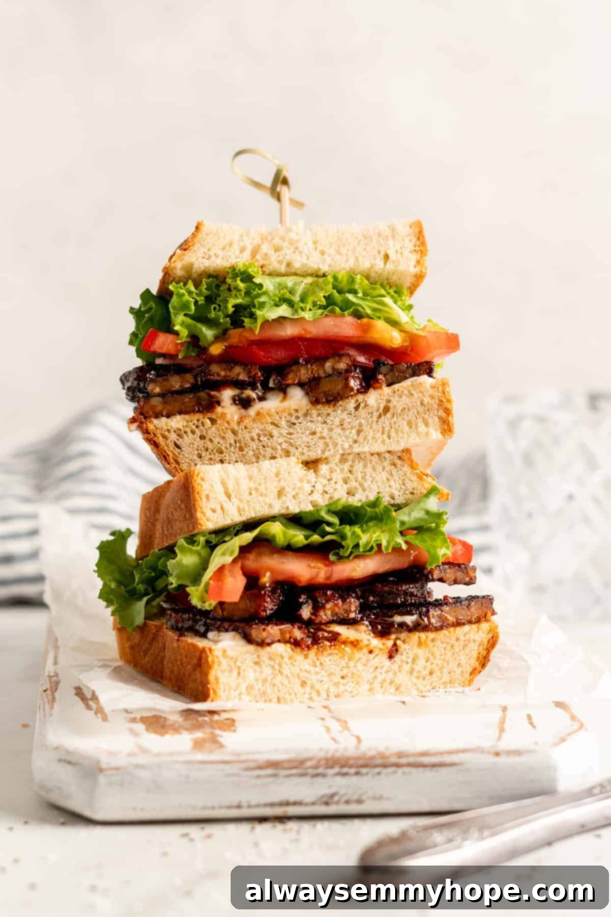 Two halves of a vegan TLT sandwich (Tempeh, Lettuce, Tomato) stacked on a wooden cutting board, showcasing the crispy tempeh bacon.