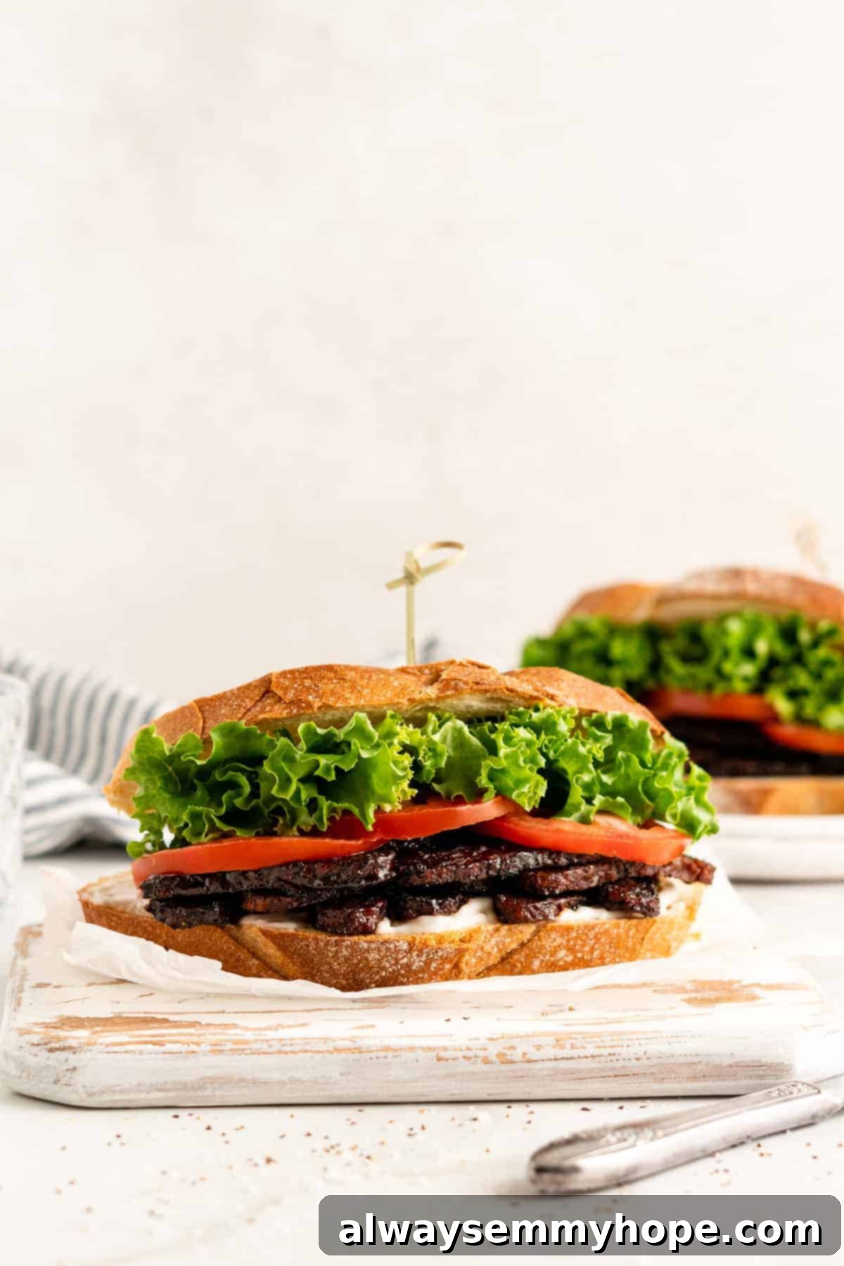 Two vegan TLT sandwiches on rustic white-painted cutting boards, showcasing the delightful tempeh bacon in a healthy meal.