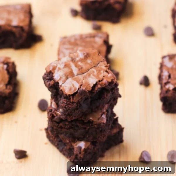 A stack of fudge brownies on a wooden table, highlighting their dense texture and delightful cracks.