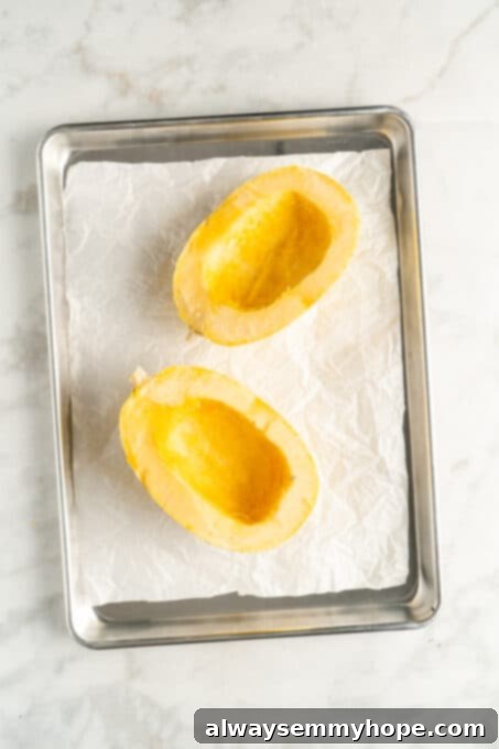 The Secret to Perfectly Cooked Spaghetti Squash 4 Overhead view of two spaghetti squash halves on a parchment-lined baking sheet, cut side up