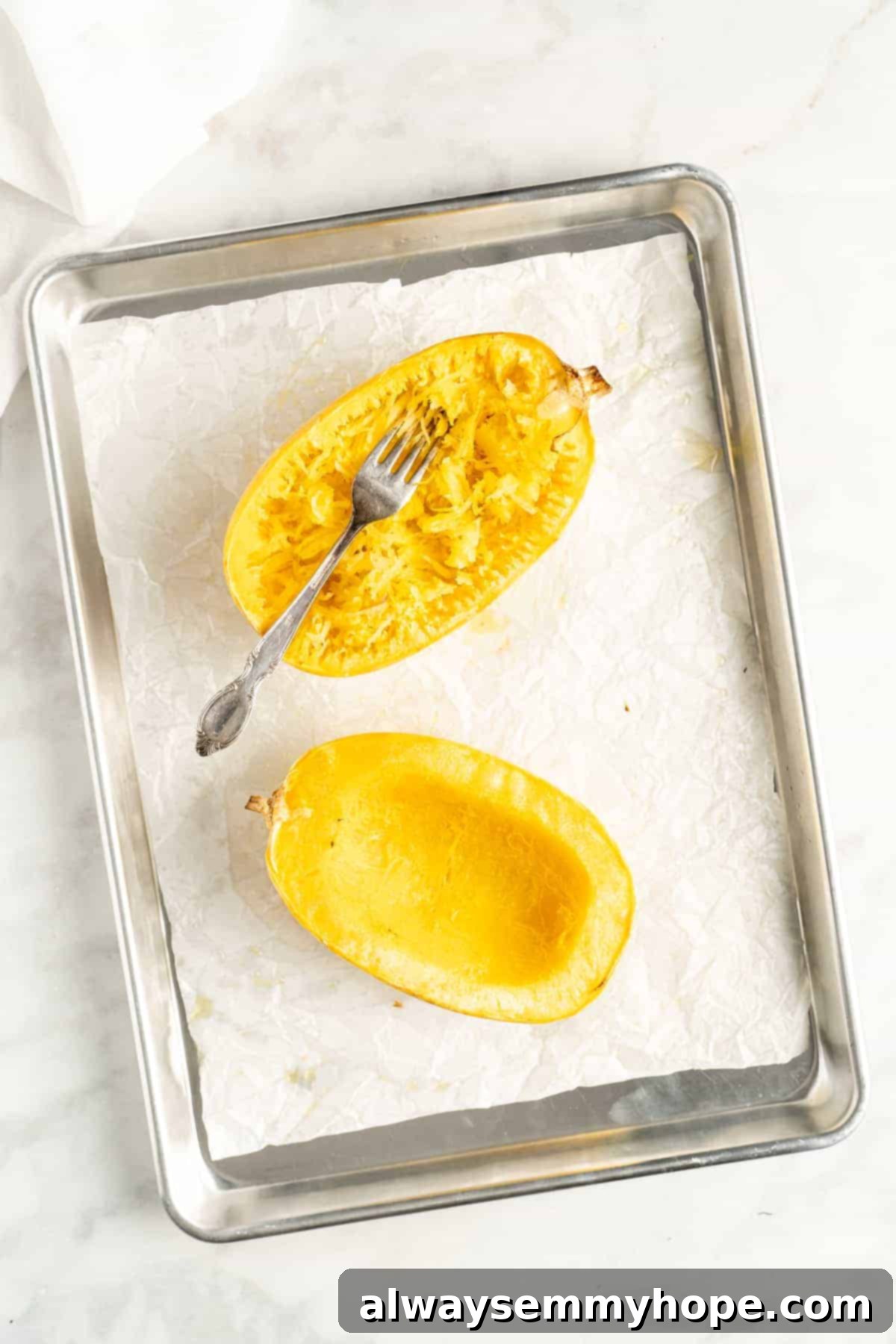 The Secret to Perfectly Cooked Spaghetti Squash 6 Overhead view of two spaghetti squash halves on a parchment lined baking sheet with a fork ready to shred