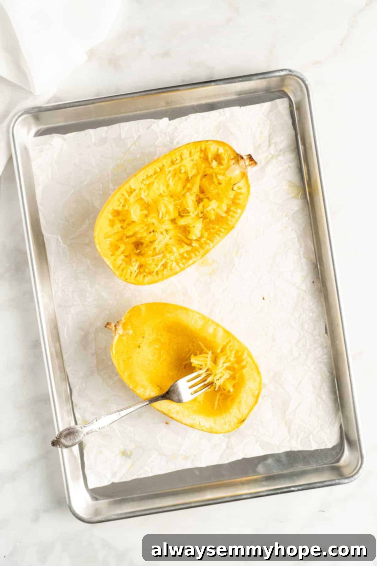 The Secret to Perfectly Cooked Spaghetti Squash 7 Overhead view of two spaghetti squash halves on a baking sheet lined with parchment paper, perfectly roasted