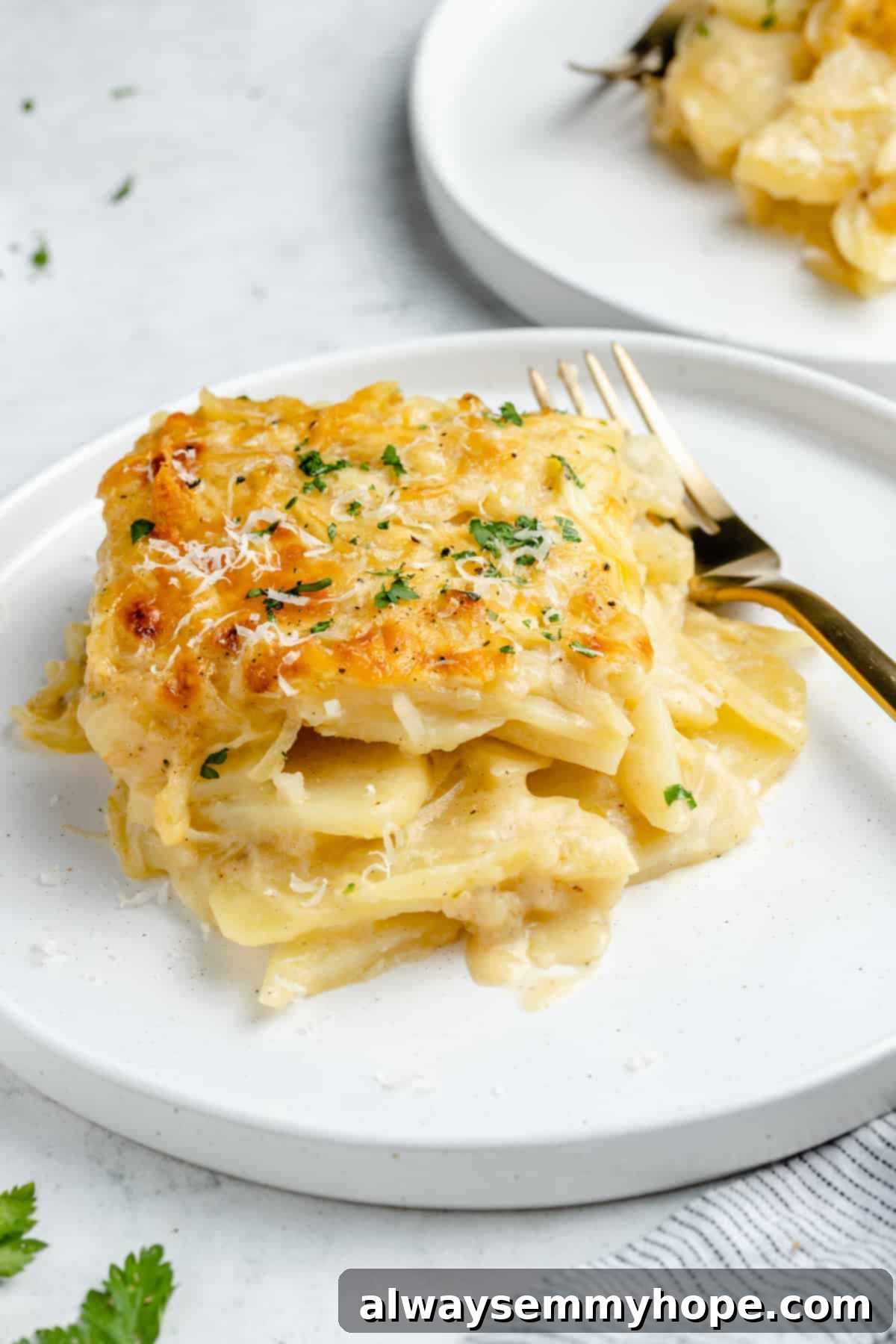 My creamy vegan scalloped potatoes are dairy-free, cheesy, and easy to make! The perfect side dish for Thanksgiving, holidays, and weeknights. Serving of scalloped potatoes on white plate with fork