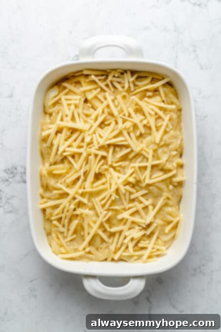 My creamy vegan scalloped potatoes are dairy-free, cheesy, and easy to make! The perfect side dish for Thanksgiving, holidays, and weeknights. Overhead view of scalloped potatoes topped with vegan cheese before baking