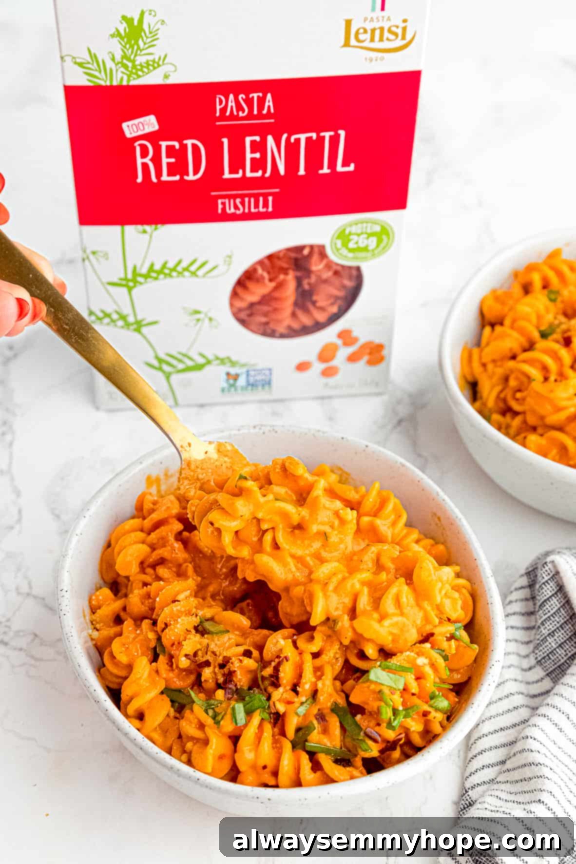 Two bowls of roasted red pepper pasta next to a box of red lentil pasta.