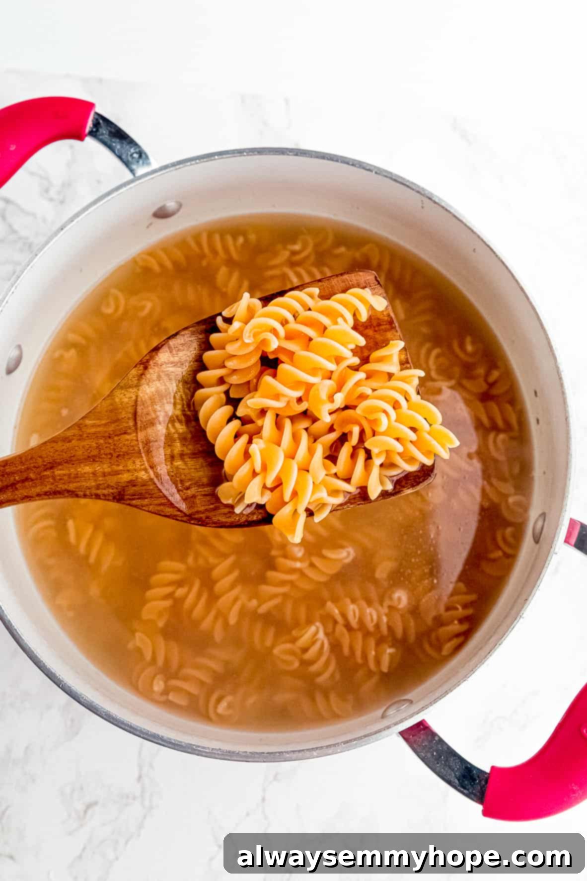 Close up of a large spoonful of cooked red lentil pasta over a pot of pasta in water.