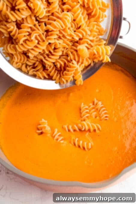 Adding cooked pasta to roasted red pepper pasta sauce in a skillet.