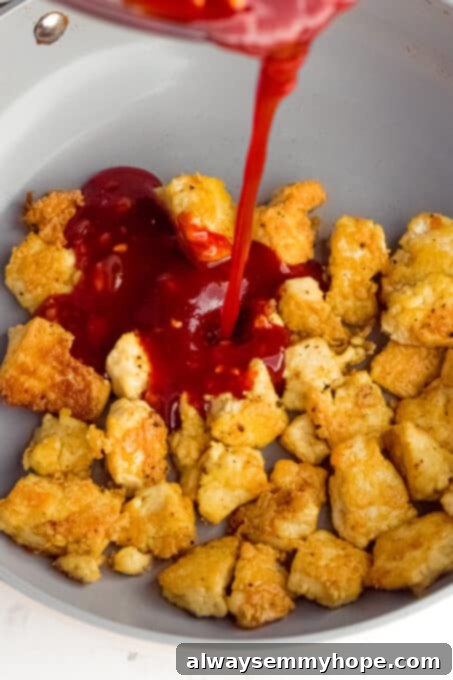 Korean Gochujang Tofu Rice Bowls 13 Crispy tofu pieces tossed with a glossy, red gochujang sauce in a pan, showcasing the final stage of cooking the tofu.