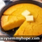 A rustic cast iron skillet filled with golden-brown corn pone, perfectly baked and garnished with pats of vegan butter, ready to be served warm.