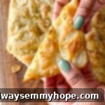 Two hands with painted nails holding a thick slice of golden-brown garlic and rosemary focaccia bread, showcasing its inviting texture.