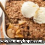A spoon digging into a warm, bubbly vegan apple crisp in a rustic baking dish, revealing the soft, spiced apple filling and crispy oat topping.