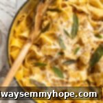Overhead view of creamy pumpkin alfredo pasta served in a skillet with a wooden spoon and garnished with a crispy sage leaf, highlighting its vibrant autumn hue.