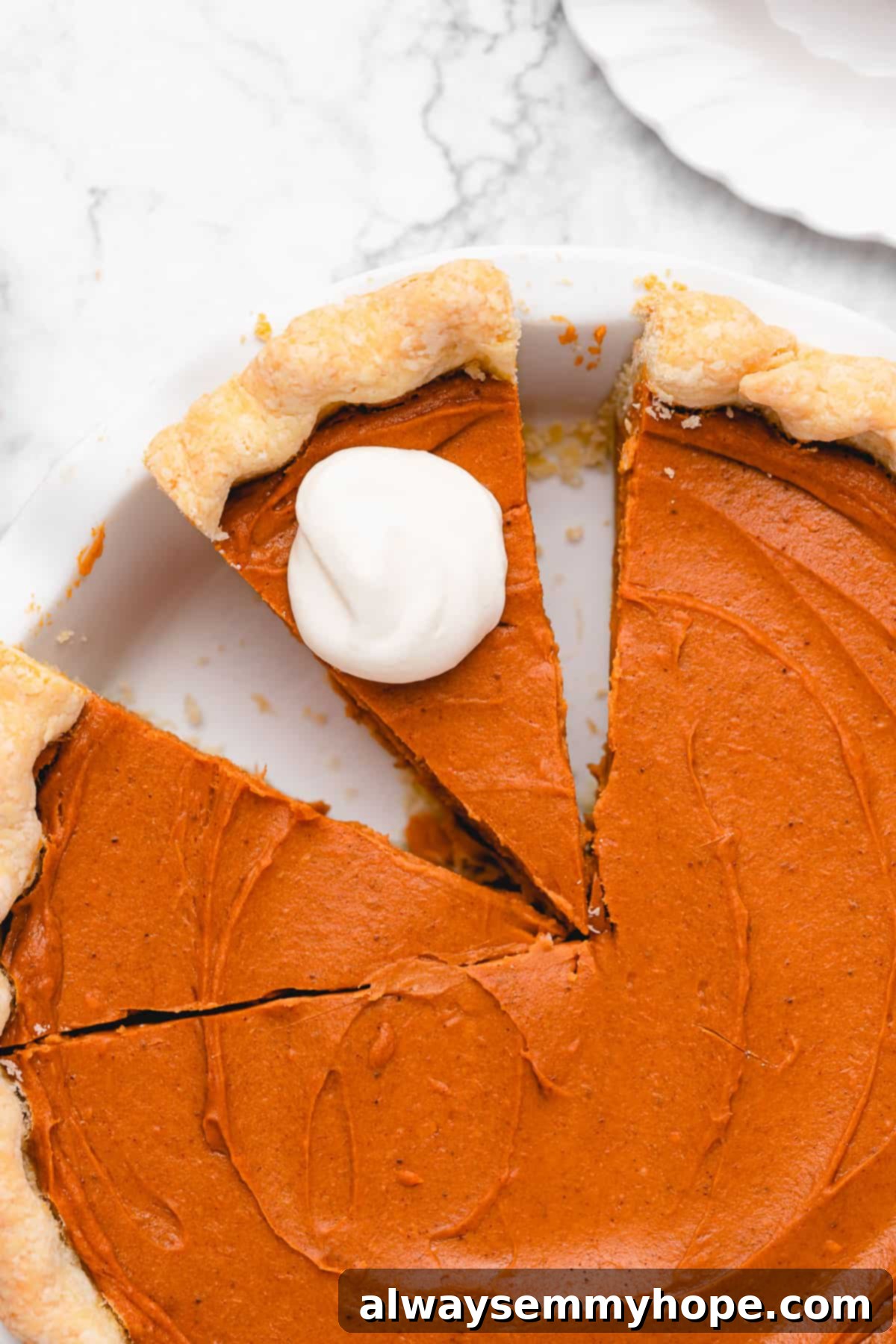 This creamy vegan sweet potato pie is easy to make with coconut milk and warm spices. It's dairy-free, egg-free, and great for Thanksgiving! An overhead shot of a freshly baked vegan sweet potato pie with two slices already cut, one of which is topped with a generous dollop of vegan whipped cream, ready to be served.