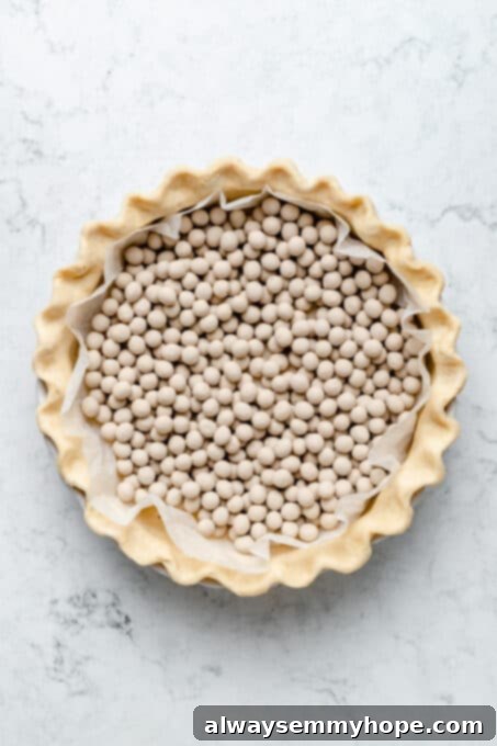 This creamy vegan sweet potato pie is easy to make with coconut milk and warm spices. It's dairy-free, egg-free, and great for Thanksgiving! A pie crust meticulously lined with parchment paper and filled with pie weights, ready for blind baking to ensure a perfectly crisp base.