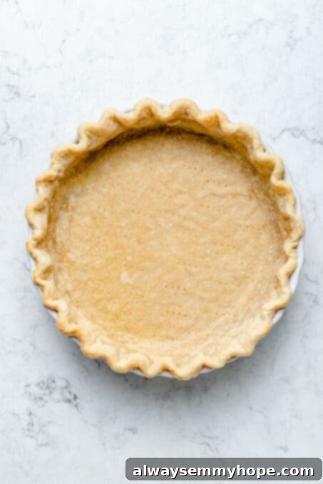 This creamy vegan sweet potato pie is easy to make with coconut milk and warm spices. It's dairy-free, egg-free, and great for Thanksgiving! A golden-brown par-baked pie crust resting in its pie plate, having just been removed from the oven and cooled, perfectly prepared for its sweet potato filling.