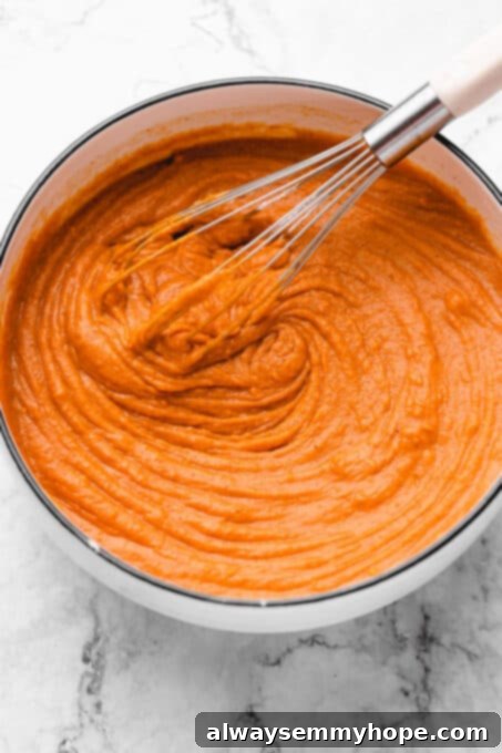 This creamy vegan sweet potato pie is easy to make with coconut milk and warm spices. It's dairy-free, egg-free, and great for Thanksgiving! A bowl of creamy sweet potato pie filling being gently whisked, illustrating the smooth texture and rich color of the batter as it rests before baking.